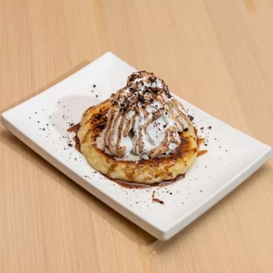 A Korean hotteok pancake topped with whipped cream, chocolate syrup, and cookie crumbles.