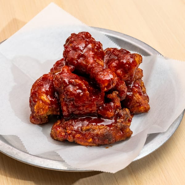 A metal plate with a pile of glossy, dark red Korean fried chicken wings on white parchment paper.