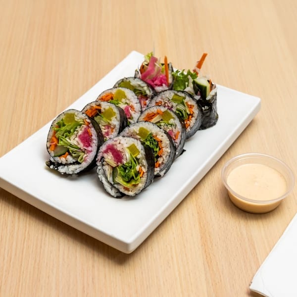 A white rectangular plate holds a row of tuna kimbap rolls with a side of sauce.
