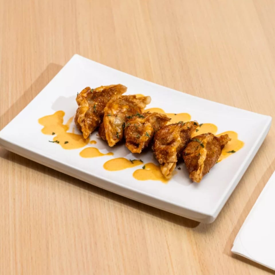 Crispy Korean fried dumplings drizzled with orange sauce and herbs on a white rectangular plate.