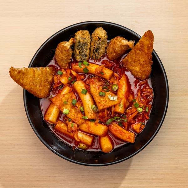 A black bowl of tteokbokki with fried dumplings, seaweed rolls, and fish cakes.