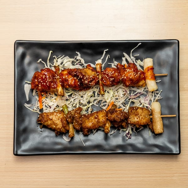 Two skewers of glazed chicken wings and two skewers of rice cakes on a bed of shredded cabbage.